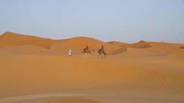 Sahra Çölü, Fas - 13 Eylül 2022: Kum tepeleri üzerinde deveyle gezen turistler, klasik bir Sahra Çölü turizmi deneyimi olan Berber bir adamın rehberliğinde