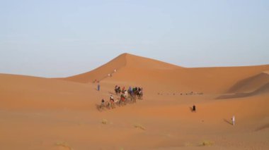 Sahra Çölü, Fas - 13 Eylül 2022: Kum tepeleri üzerinde deveyle gezen turistler, klasik bir Sahra Çölü turizmi deneyimi olan Berber bir adamın rehberliğinde
