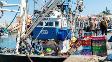 Essaouira, Fas - 17 Eylül 2022: Geleneksel mavi balıkçı teknesinde balıkçılar yelkenden dönüyorlar ve günün avını Essaouira limanına getiriyorlar