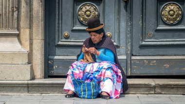 Cusco, Peru - 24 Ekim 2023: Geleneksel giysili Perulu kadın caddenin karşısındaki kapının önünde örgü örüyor