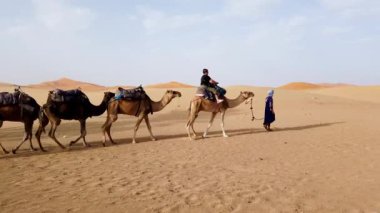 Sahra Çölü, Fas - 13 Eylül 2022: Kum tepelerinde deveyle gezen bir turist Berber bir adamın rehberliğinde, klasik bir Sahra Çölü turizmi deneyimi