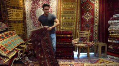 İsfahan, İran - 12 Mayıs 2023: İran halılarını turistlere sunan yakışıklı İran halıcısı