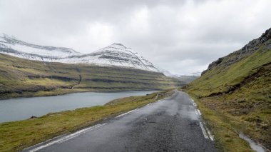 Faroe Adaları 'nda uzak bir yol, fiyort ve kar kaplı dağlardan oluşan büyük bir manzarayla açılır. Virajlı yollarda giderken Faroe Adası 'nın manzarası dinamik bir paletle değişir.