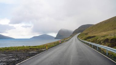 Faroe Adaları 'nda uzak bir yol fiyort ve sisli dağların manzarasıyla açılır. Virajlı yollarda giderken Faroe Adası 'nın manzarası dinamik bir paletle değişir.