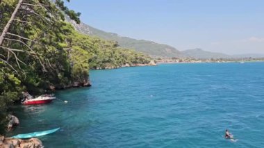 Akyaka, Mugla, Türkiye - 31 Temmuz 2023: Akyaka köyünün deniz kıyısında yüzen insanlar, manzaralı kıyı şeridi ve çarpıcı doğal çevresiyle popüler turistik beldeler