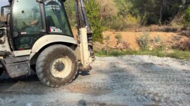 Mugla, Turkey - March 2022: Mini bulldozer clearing forest for new road construction, levelling and moving soil during road building. Dozer clearing small twigs and branches.