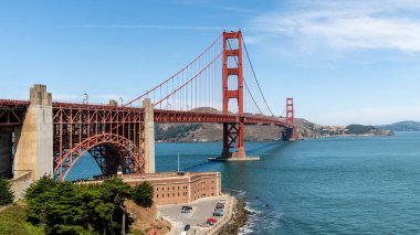 Golden Gate Köprüsü güneşli bir yaz gününde San Francisco Körfezi boyunca uzanır, canlı kırmızı tonunu ve çarpıcı mimari tasarımını sergiler..