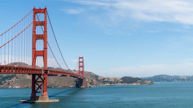 Golden Gate Köprüsü güneşli bir yaz gününde San Francisco Körfezi boyunca uzanır, canlı kırmızı tonunu ve çarpıcı mimari tasarımını sergiler..