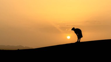 Sahra Çölü, Fas 'taki güzel günbatımında kum tepelerinde dua eden kimliği belirsiz Müslüman Berberi silueti.