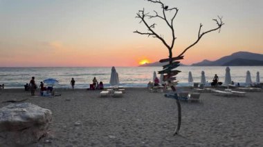 Oludeniz, Mugla, Türkiye - 24 Ağustos 2024: Gün batımında plajda oturan bir grup insan. Manzara huzurlu ve rahatlatıcı..