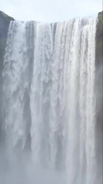 Skogafoss şelalesinin yakın çekimi İzlanda 'da kayalık kayalıklardan aşağı yuvarlanırken, yemyeşil ve doğanın nefes kesici güzelliğini gözler önüne seriyor. Dikey video