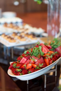 Taze çilek ve sebzeler diğer yiyeceklerin yanında bir masada duruyor, canlı ve iştah açıcı bir görüntü yaratıyor..