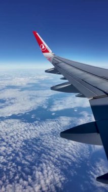 İstanbul, Türkiye - 15 Kasım 2024: Türk Havayolları uçağının kanadında ikonik kırmızı logosu, uluslararası bir yolculukta bulutların üzerinde uçuyor.
