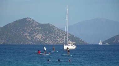 Mugla, Türkiye - 11 Ekim 2024: Akdeniz 'de yaz su sporları ve tatil eğlencesi için mükemmel bir yer olan Dalaman' ın Sarsala Körfezi 'nin sakin sularında stand-up sörfü yapan insanlar