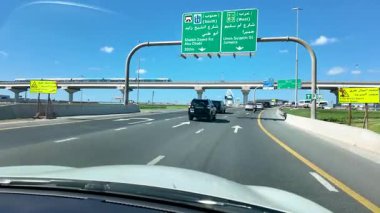 Dubai, BAE - 13 Kasım 2024: Dubai şehir caddesinde arabaların, trafik levhalarının ve modern şehir manzaralarının altında güpegündüz çekilmiş POV görüntüleri.