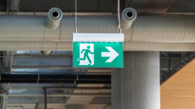 Çıkış tabelasında, tavandan sarkan ve acil tahliye yolunu gösteren bir ok var. Binalarda evrensel bir güvenlik sembolü.