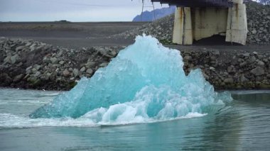 Eriyen bir buz bloğunun yavaş hareketi Jokulsarlon buzulu lagününden okyanusa doğru sürüklenir. İklim değişikliğinin çarpıcı bir hatırlatıcısı ve küresel ısınmanın etkisi.