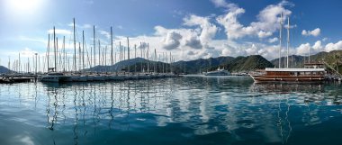 Gocek, Türkiye - 3 Kasım 2024: Turkuaz Akdeniz 'e demirlemiş yelkenli ve lüks yatları olan Gocek Marina, yemyeşil dağlar ve canlı bir kıyı kasabasıyla çevrili.