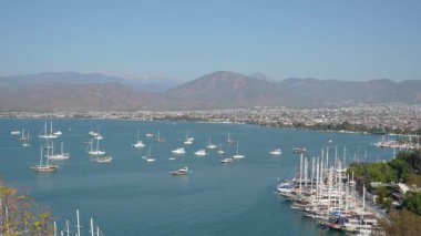 Fethiye Yat Marina 'nın turkuaz Akdeniz' de demirli, yemyeşil dağlarla çevrili yelkenli ve lüks yatlarıyla hava manzarası ve canlı bir sahil kasabası..