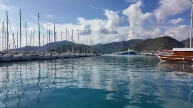 Gocek, Türkiye - 3 Kasım 2024: Turkuaz Akdeniz 'e demirlemiş yelkenli ve lüks yatları olan Gocek Marina, yemyeşil dağlar ve canlı bir kıyı kasabasıyla çevrili.