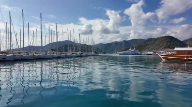 Gocek, Türkiye - 3 Kasım 2024: Turkuaz Akdeniz 'e demirlemiş yelkenli ve lüks yatları olan Gocek Marina, yemyeşil dağlar ve canlı bir kıyı kasabasıyla çevrili.