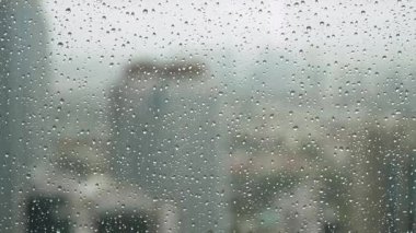 Cama yapışmış su damlacıklarıyla dolu bir pencereden yağmurlu bir gün manzarası dışarıdaki şehir manzarasını bulanıklaştırıyor, sakin ve içsel bir ruh hali yaratıyor.