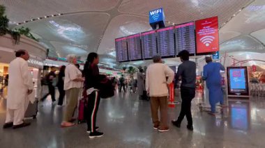 İstanbul, Türkiye - 13 Temmuz 2025: Türkiye 'deki yoğun İstanbul Havalimanı terminalinde uçuş bilgileri panosunu kontrol eden yolcuların zaman aşımı