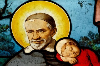 Paris, FRANCE - 09-11-2024: Kollarında bir çocuk taşıyan St. Vincent de Paul 'un lekeli camları. Roma Katolik Kilisesi 'nin azizi..