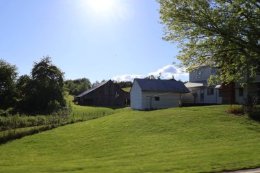 Güneşli bir günde arka planda ağaçlar ve ahır olan güzel bir çiftlik evi manzarası..