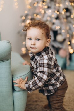 Kıvırcık bir çocuk Noel ağacının yanında evde vakit geçiriyor.