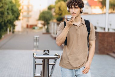 Çekici kıvırcık saçlı genç üniversite ya da kampüste sesli mesaj kaydeden üniversite öğrencisi.