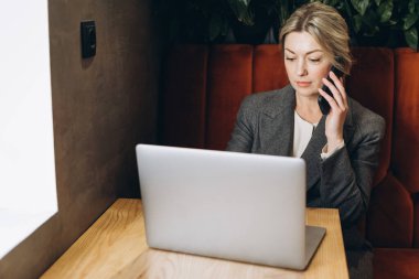 Olgun iş kadını restoran yöneticisi telefonda konuşuyor ve dizüstü bilgisayarla çalışıyor.