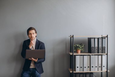 Modern ofiste takım elbiseli ve dizüstü bilgisayar kullanan genç ve neşeli iş adamının görüntüsü