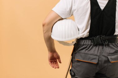 Bej arka planda kask tutan erkek inşaat işçisi.