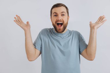 Mavi tişörtlü, modern sakallı orta yaşlı bir adamın portresi, beyaz arka plandaki duyguları bilmediğini gösteriyor.