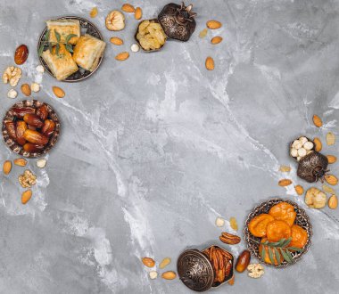 Geleneksel Arap sofra takımı ve yemek takımlarıyla süslü afiş, bir fincan çay, Kuran ve gri taşlı arka planda tespih. Ramazan masa üstü görünümü