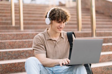 E-öğrenme, uzaktan öğrenme veya uzaktan öğrenme kavramı, üniversitede basamaklarda dizüstü bilgisayar kullanan genç kıvırcık saçlı okul çocuğu, üniversite ya da üniversite öğrencisi