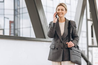Takım elbiseli, gri ceketli, güzel bir iş kadınının portresi modern şehir arka planında gülümseyen ve konuşan.