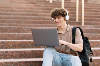 E-öğrenme, uzaktan öğrenme veya uzaktan öğrenme kavramı, üniversitede basamaklarda dizüstü bilgisayar kullanan genç kıvırcık saçlı okul çocuğu, üniversite ya da üniversite öğrencisi