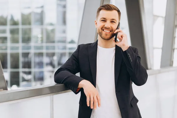 都市部の建物やオフィスの背景に電話で話して訴訟でハンサムな幸せな男性ビジネスマンの肖像画 — ストック写真