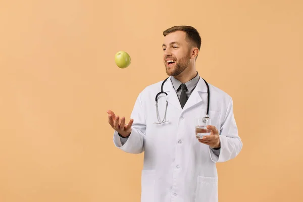 Lekarz Dietetyk Męski Stetoskopem Uśmiechający Się Trzymający Wodę Jabłko Beżowym — Zdjęcie stockowe