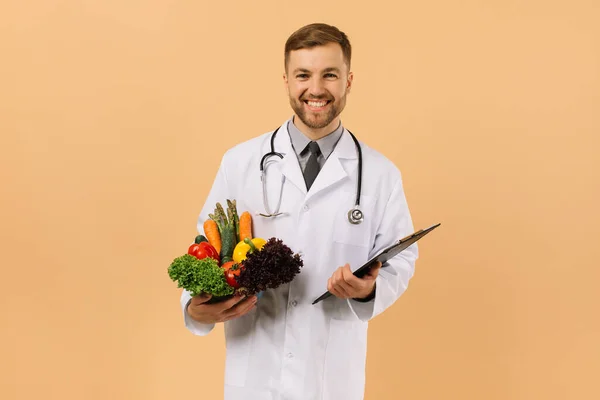 Médico Nutricionista Masculino Com Estetoscópio Segurando Legumes Frescos Fundo Bege — Fotografia de Stock