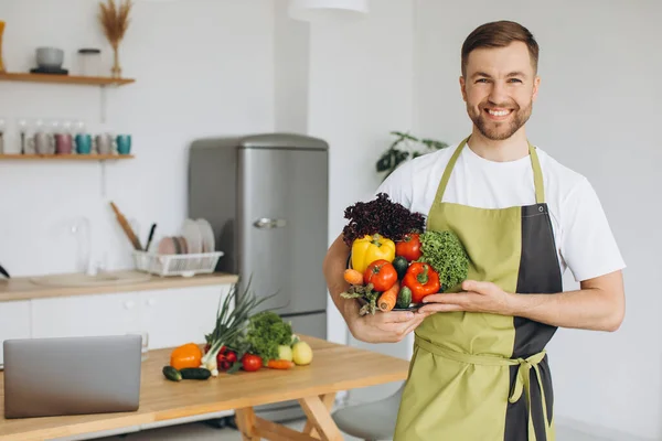 stock image Portrait of a happy man holding a plate of fresh vegetables on the background of the kitchen at home