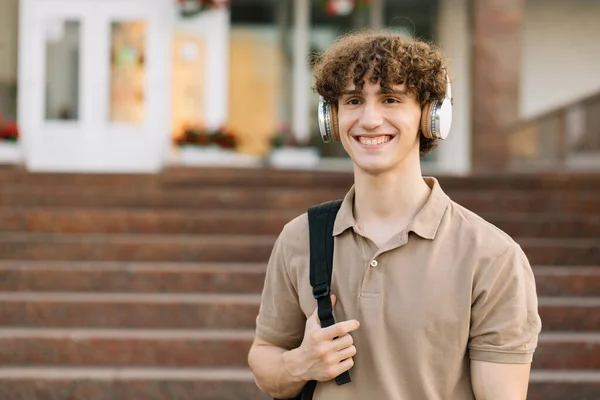 Çekici Kıvırcık Saçlı Kulaklıklı Gülümseyen Erkek Öğrencinin Portresi — Stok fotoğraf