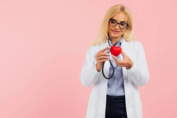 熟女医師でガラスとともに聴診器保持心臓上のピンクの背景にコピースペース — ストック写真