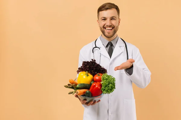 聴診器付きの幸せな男性医師栄養士はベージュの背景に新鮮な野菜を示しています 食事計画の概念 — ストック写真