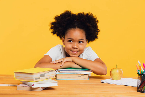 Happy African American schoolgirl sitting at desk leaning on books. Back to school concept.