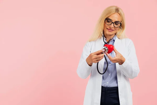 熟女医師でガラスとともに聴診器保持心臓上のピンクの背景にコピースペース — ストック写真