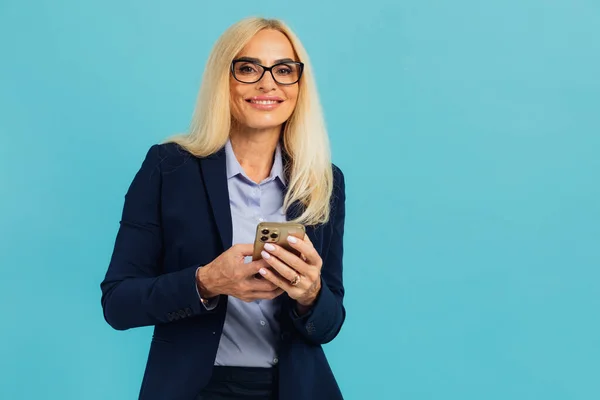 Piękna Dojrzała Kobieta Garniturze Biznesowym Okularach Trzymać Telefon Odizolowanym Niebieskim — Zdjęcie stockowe