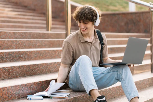 电子学习的概念 远程学习或远程学习的概念 年轻快乐的卷发男 带着背包和耳机的大学生 坐在大学的台阶上 — 图库照片